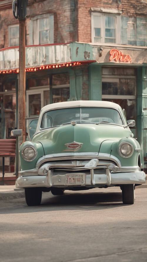 Um carro antigo dos anos 1950 em verde salva desbotado estacionado em frente a uma antiga lanchonete.