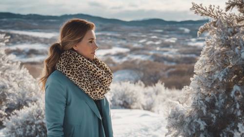Duży, luksusowy szalik z nadrukiem geparda owinięty wokół szyi kobiety, która patrzy na śnieżny krajobraz.
