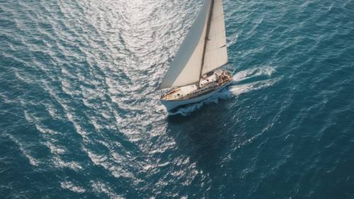 An aerial view of a sailboat cruising on a sparkling blue sea.