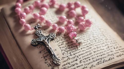 An ornate pink rosary resting on a well-loved prayer book. Tapet [e0c06345011347e5ab2c]