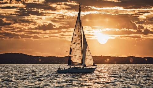 An orange and white sailboat on a calm sea with the sun setting.