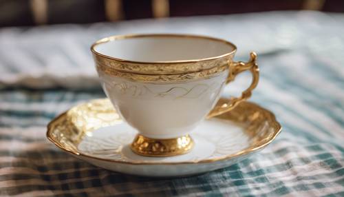 Delicata tazza da tè con piattino a strisce dorate, contro una tovaglia in stile vittoriano.