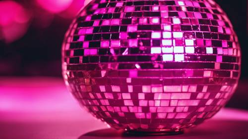 A focus on a shiny metallic disco ball reflecting hot pink lights.