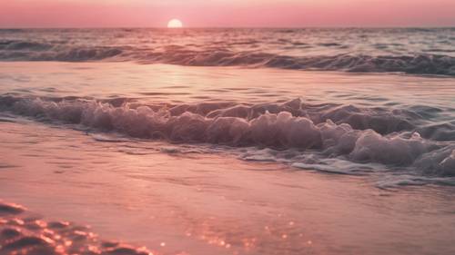 A blush pink, summer sunrise reflecting off the gentle waves of a serene beach.