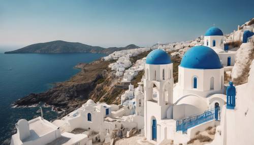 A white-washed church with blue-domed roofs located hilltop, overseeing the deep blue Aegean Sea.