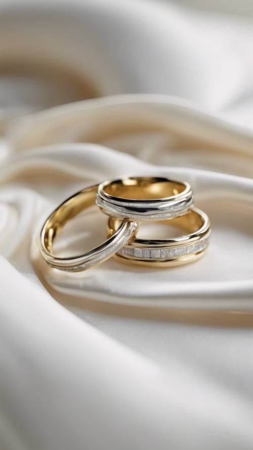 A pair of golden and silver wedding rings intertwined on a white silk pillow.