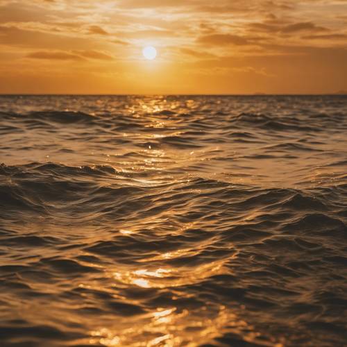 Matahari terbenam berwarna kuning dan emas cerah di atas laut yang damai.