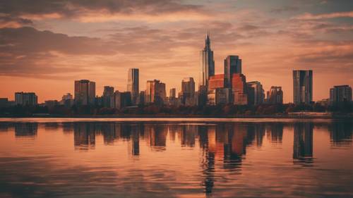 The city skyline reflecting off a lake under a calm sunset, the color palette shifting towards warm hues of fall.