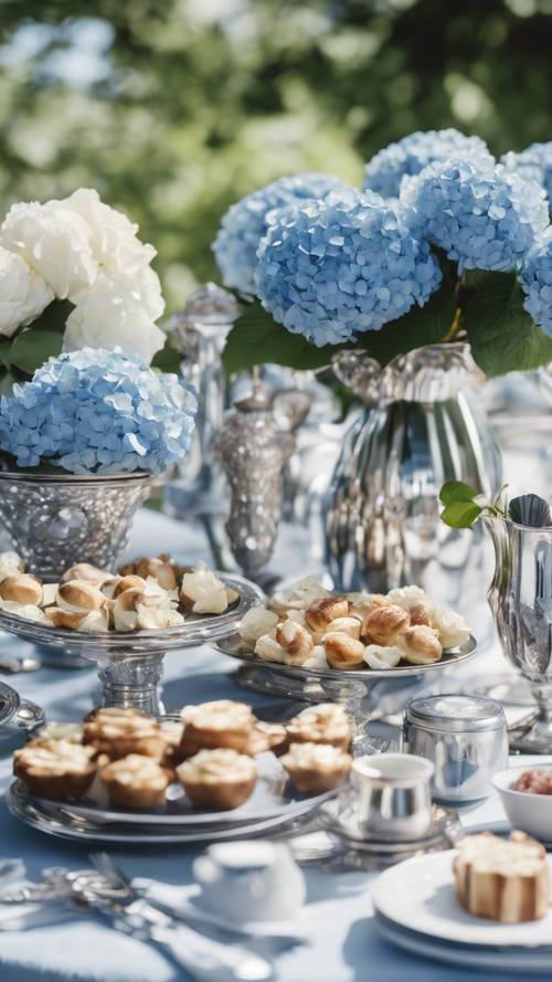 A sumptuous summer brunch spread on a preppy styled table, with clusters of blue hydrangeas and white roses in silver vases.