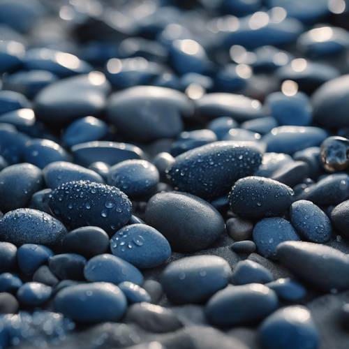 Nahaufnahme von dunkelblauen Kieselsteinen mit strukturierter Struktur an einem Strand, auf denen Wassertropfen glitzern.