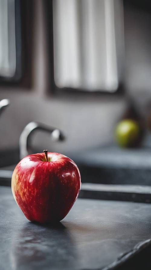 A vibrant red apple sitting on a gray slate countertop.