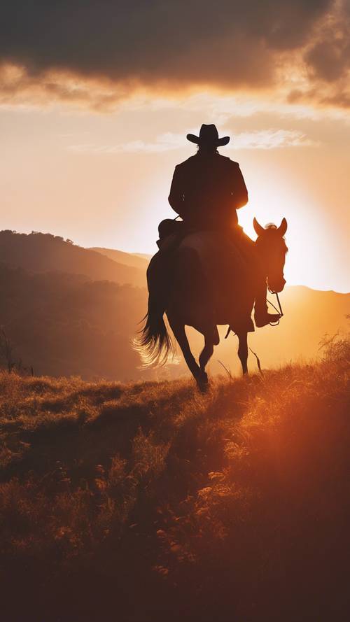 Une silhouette d&#39;un cowboy sur son cheval au sommet de la colline pendant un coucher de soleil éclatant.
