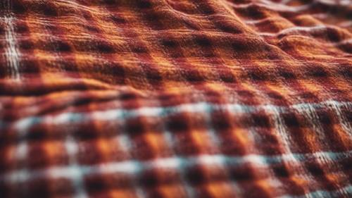 Un patrón de cuadros rojos y naranjas tejido en una manta campestre desgastada.