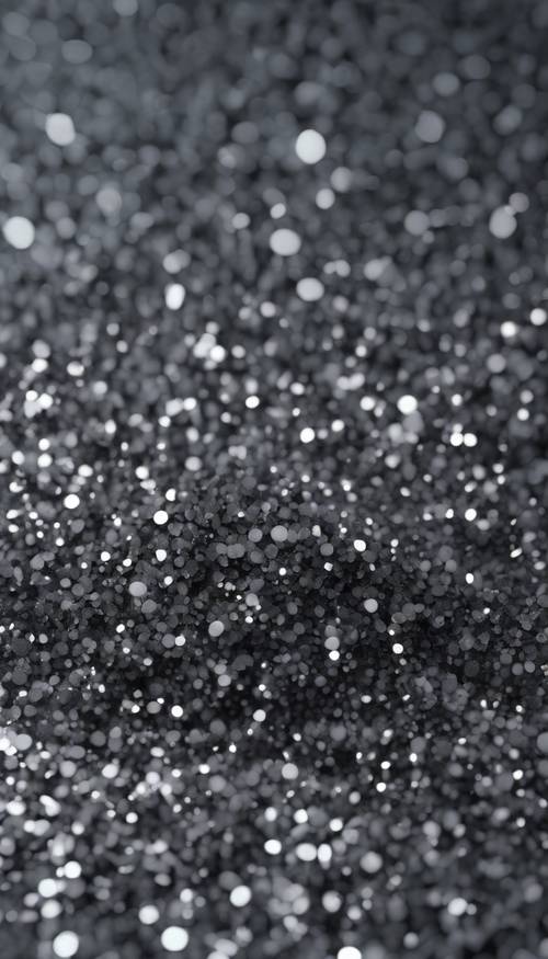 A close-up view of dark gray glitter particles densely scattered, creating a seamless texture under subtle lighting.