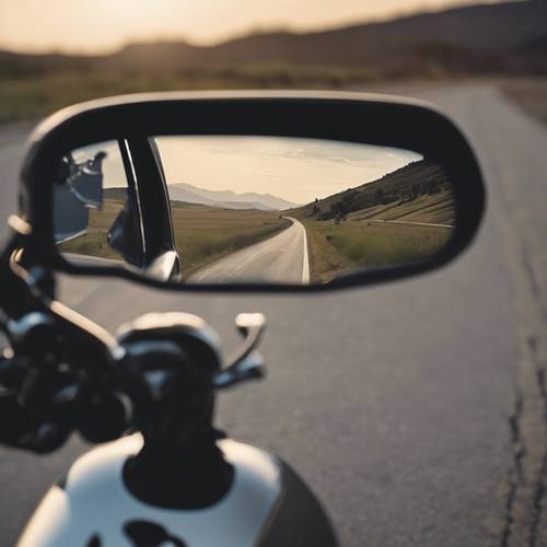 The rearview mirror of a motorcycle showing the open road behind.
