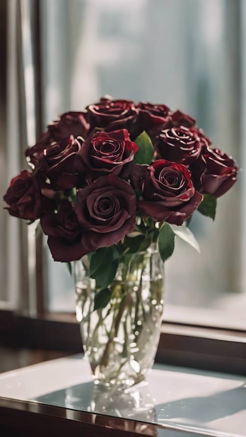 Buket mawar merah marun gelap dihiasi bunga lili putih kecil di atas meja kaca.