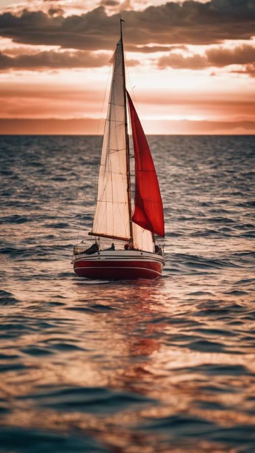 A red boat with a white sail sailing in the open ocean during sunset.