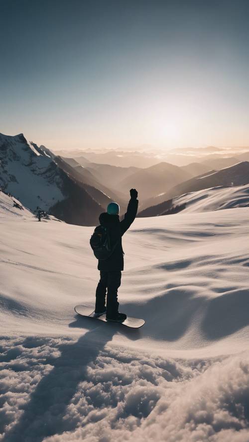 Silhouette of a snowboarder holding his board aloof, standing triumphant at the peak of a mountain at dusk.