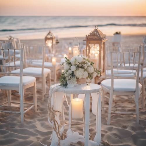 White boho wedding decor with hanging lanterns and crisp white chairs on a beach at sunset.