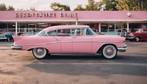 Розовый классический автомобиль, припаркованный на стоянке у закусочной в стиле 50-х годов.