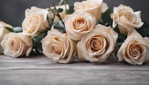 Ein Strauß beiger Rosen auf einem grauen Holztisch.