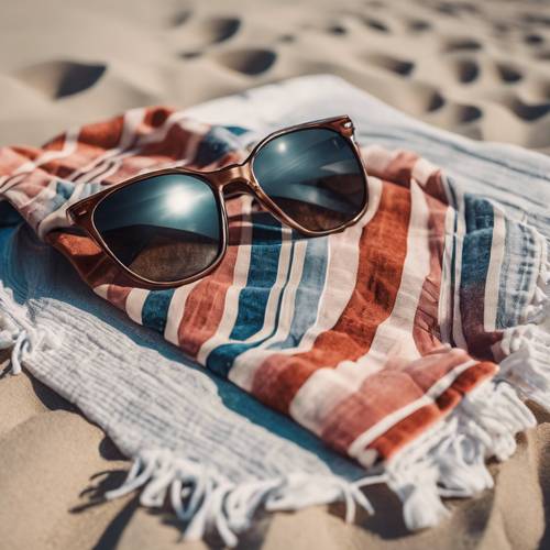 Ręcznik plażowy w stylu preppy rozłożony na plaży z parą ekstrawaganckich okularów przeciwsłonecznych.