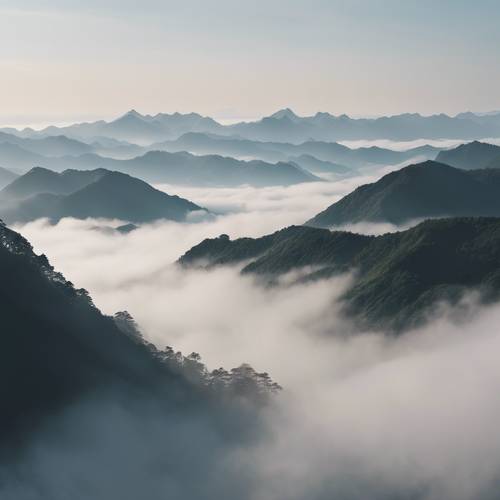 Uma foto aérea da neblina rolando suavemente pelos picos de uma montanha japonesa.