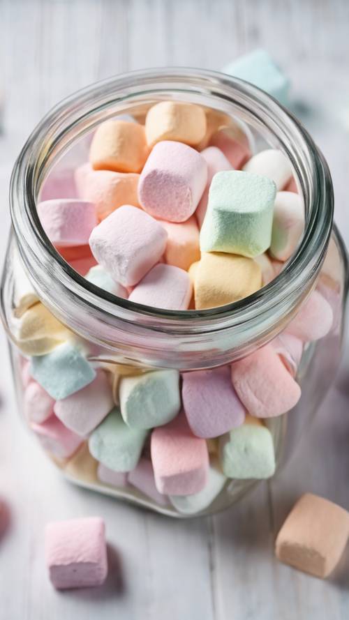Un barattolo di marshmallow gourmet di vari colori pastello, ripreso dall&#39;alto con uno sfondo di tavolo in legno bianco.