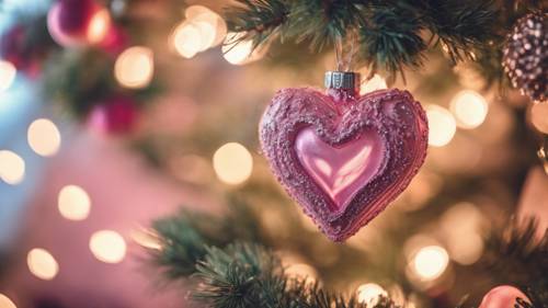 Ein rosafarbenes herzförmiges Ornament, das an einem üppigen Weihnachtsbaum hängt.