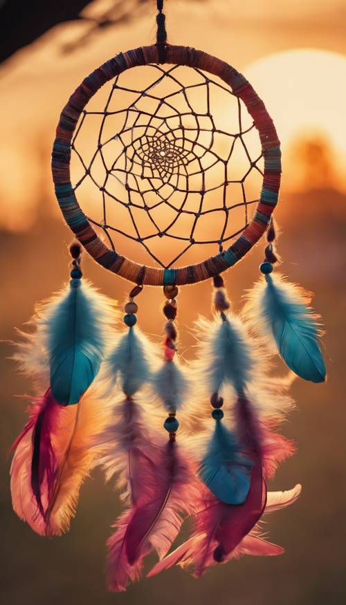 A close-up of a colourful dreamcatcher, with vibrant feathers and intricate weaving against a sunset backdrop. Tapeta [ddd1e6d7867049d3bf25]