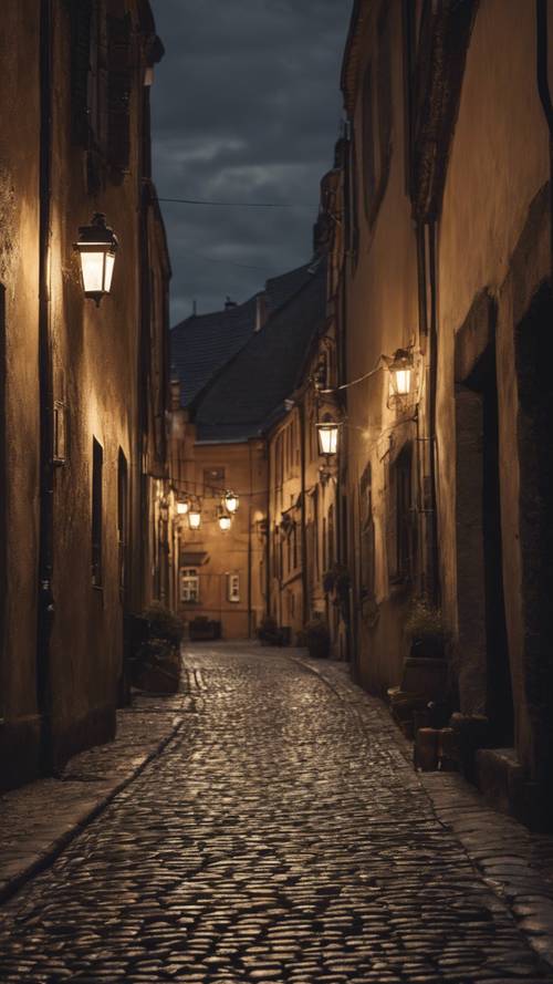 Cicha, ciemna, brukowana uliczka w starym europejskim mieście, oświetlona jedynie przyćmionymi, migoczącymi latarniami. Tapeta [2b865b8c868740aeb53a]