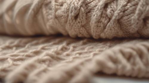 A close view of a texture-rich, beige woolen sweater with knitting needles.
