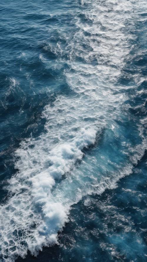 Una vista aérea de primer plano del mar azul profundo con olas blancas y espumosas que azotan la orilla.
