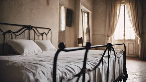 빈티지 철제 침대 위에 뽀송뽀송한 리넨 시트가 있는 프로방스 스타일의 인테리어 장면입니다.