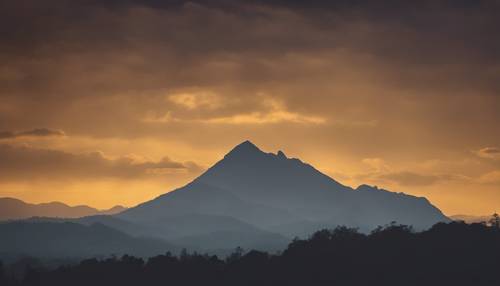 A silhouette of a mountain against a dark yellow dusk sky.