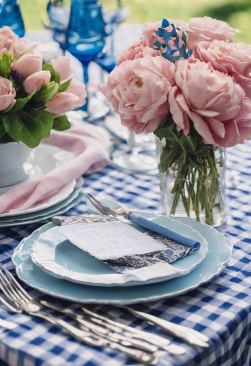 Mesa para fiesta de cumpleaños con temática preppy, con mantel de cuadros azules, centro de mesa floral a juego y elegantes cubiertos plateados.