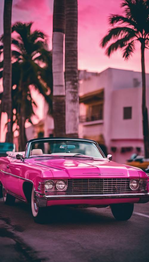 A neon pink vintage convertible parked on the streets of Miami at sunset.