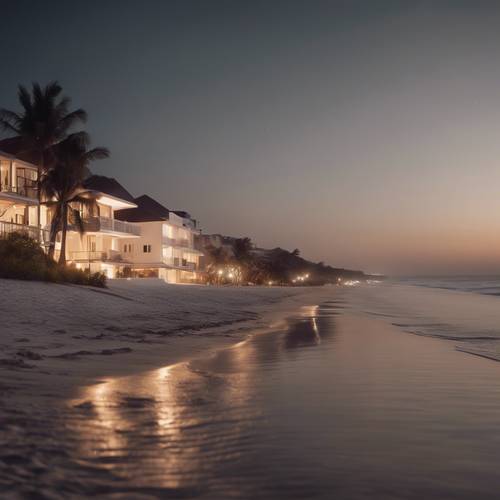 Biała plaża nocą, oświetlona delikatnym blaskiem odległych domów przy plaży.
