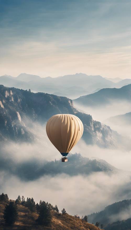 Um balão de ar quente bege e azul voando acima dos picos das montanhas enevoadas.