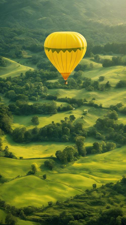 A vibrant yellow hot air balloon floating above green mountains.