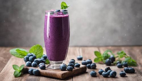 A blueberry smoothie in a tall glass garnished with a fresh mint leaf.