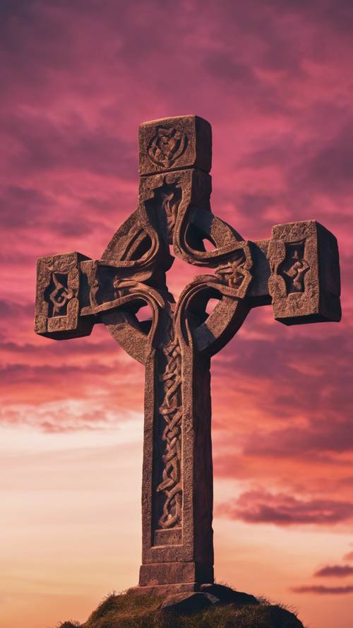 A large Celtic stone cross silhouetted against a dramatic sunset, the orange and pink hues of the sky coloring the landscape.
