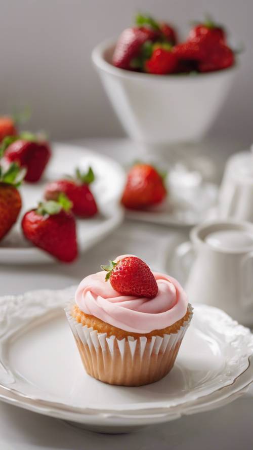 Ein einzelner Erdbeer-Cupcake auf einem weißen Porzellanteller im hellen Tageslicht.
