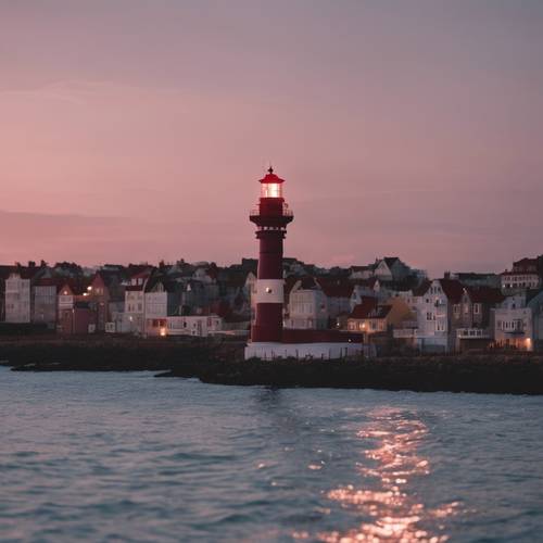 A maroon lighthouse visible at a distance against the backdrop of a quiet seaside town during dusk.