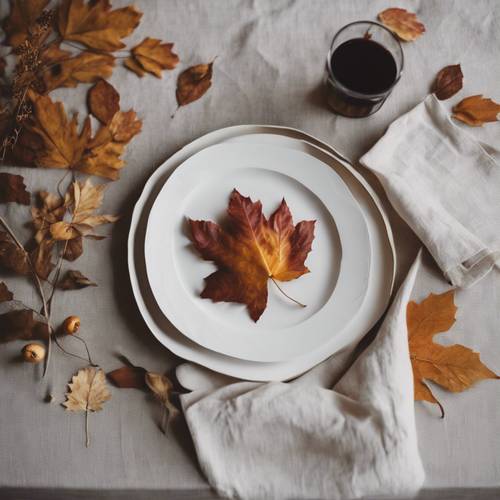 Decoração de mesa de Ação de Graças para amantes da simplicidade com pratos brancos minimalistas, guardanapos de linho natural e algumas folhas de outono espalhadas.