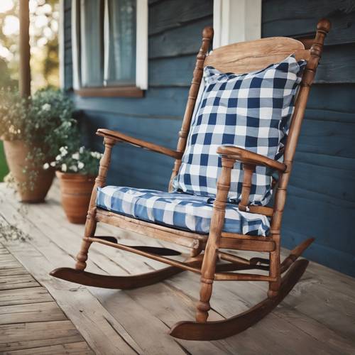 Une chaise à bascule ancienne mais charmante avec un coussin à carreaux bleu et blanc fait main sur un porche en bois.