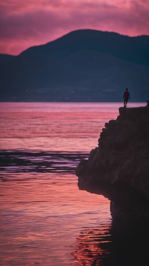 A lone cliff diver poised for the jump against a vibrant twilight sky.