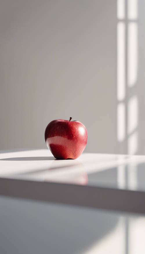 תפוח אדום בודד ופריך יושב על משטח שולחן נקי ולבן, אור השמש מאיר אותו.