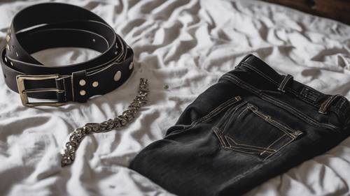 Un jean skinny noir, une ceinture cloutée et un t-shirt de groupe sont disposés sur un lit, prêts à être portés.