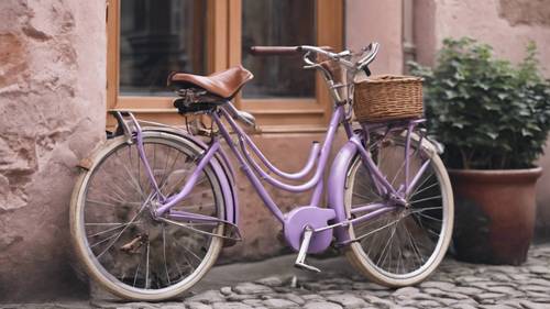 Sepeda vintage berwarna ungu pastel bersandar di dinding batu besar.